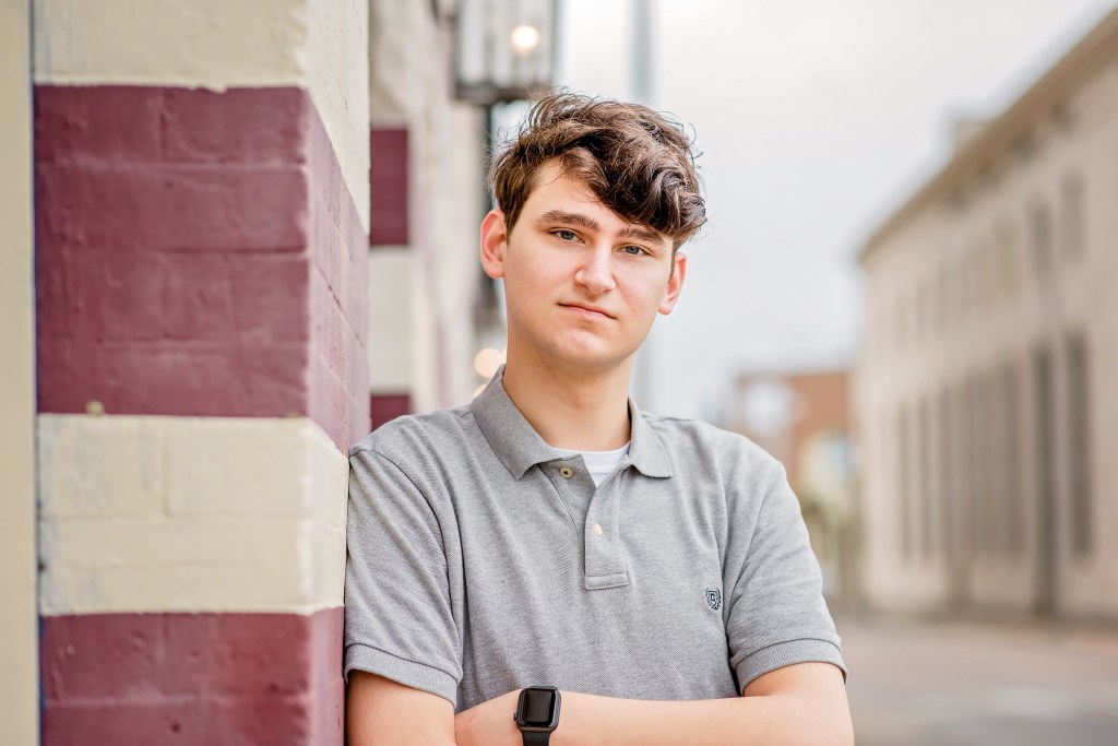 An Image of Kaden Marshall. His arms are crossed and he's leaning against a brick wall.